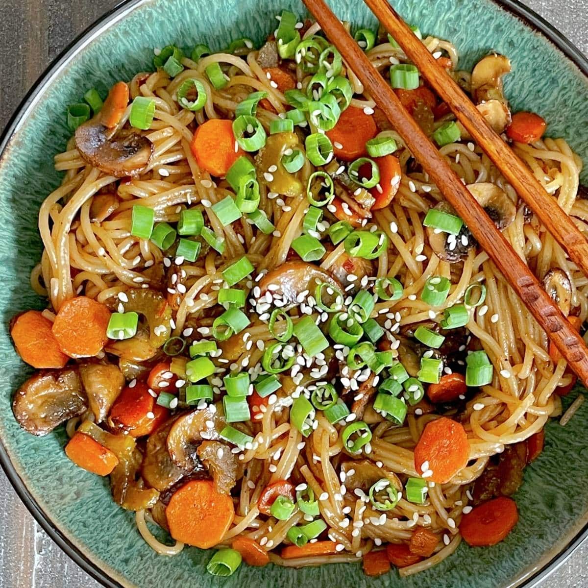 Bowl of sautéed rice noodles with carrots and green onions.