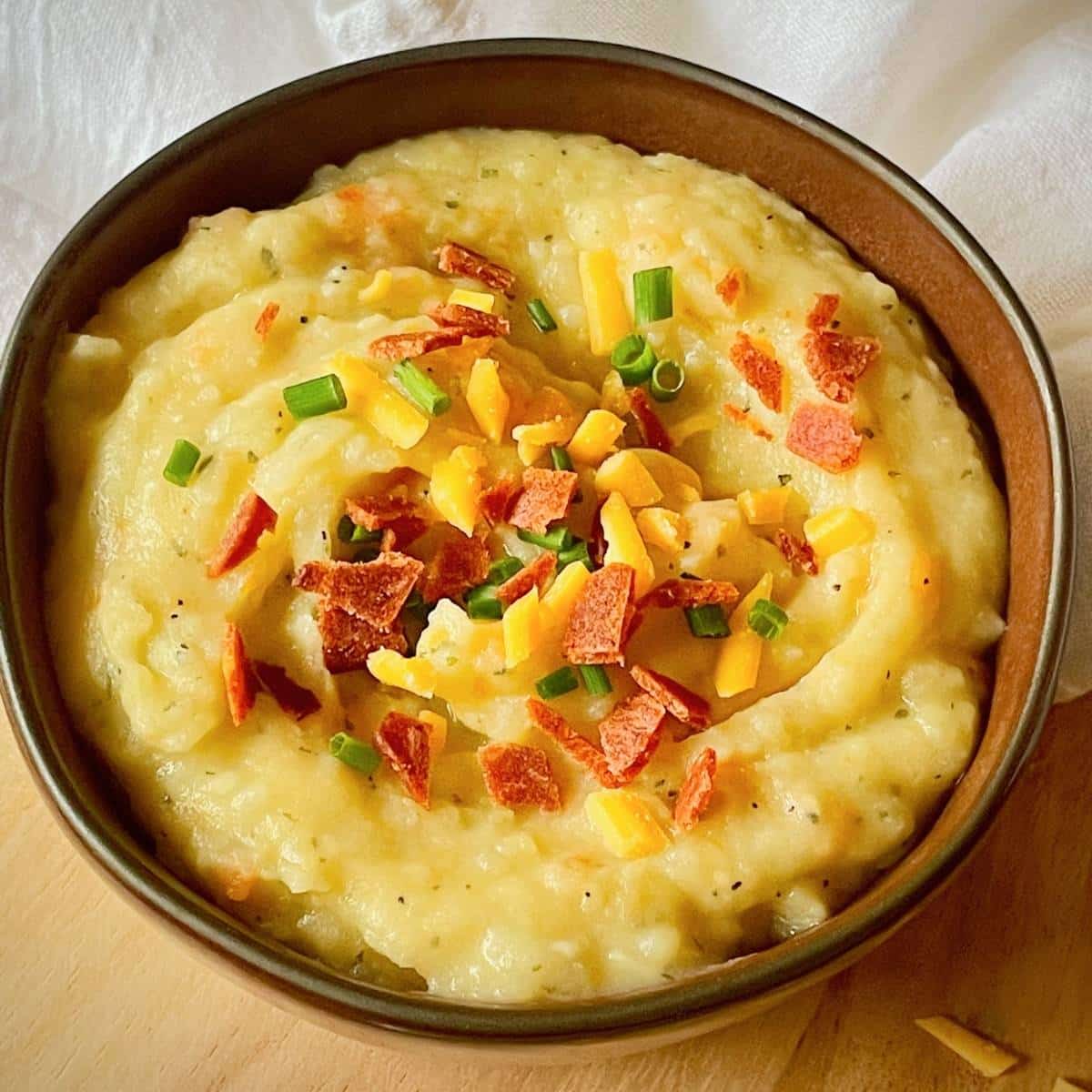 Bowl of vegan potato soup, topped with vegan bacon, chives, and vegan cheddar.