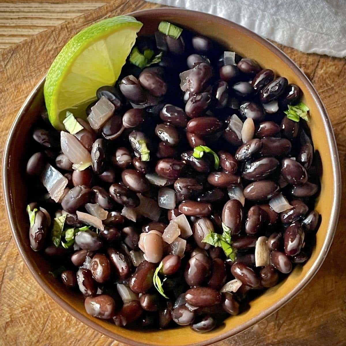 A bowl of black beans with a lime wedge as garnish.