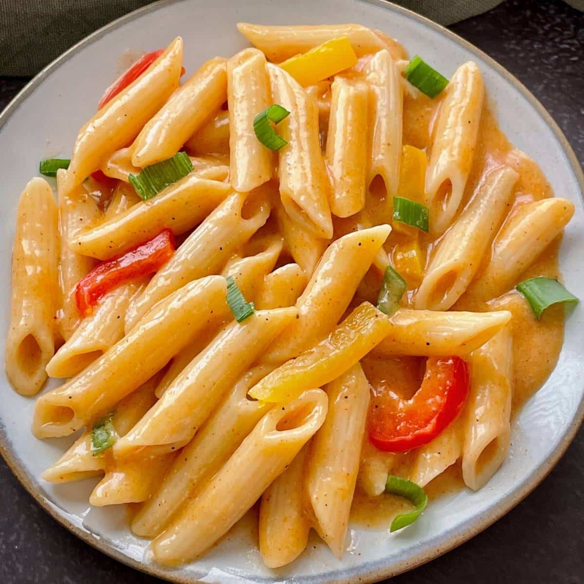 cooked vegan cajun pasta with peppers and green onions, on a white plate