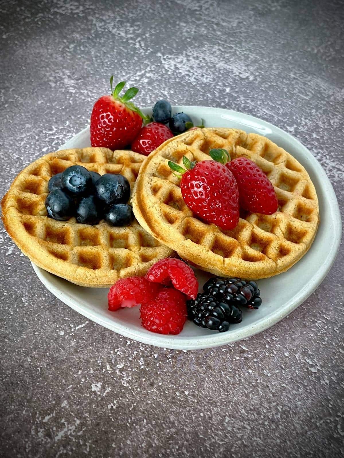 Cooked waffles on a plate with fresh fruit.