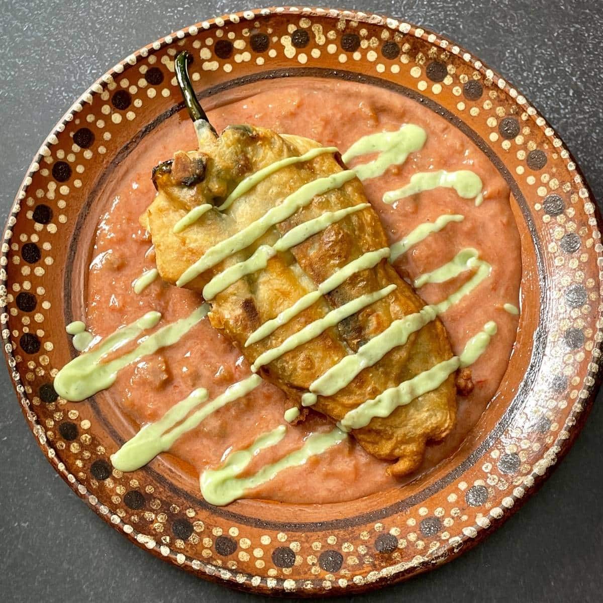 Vegan chile relleno on top of red chile sauce and topped with avocado cream sauce.