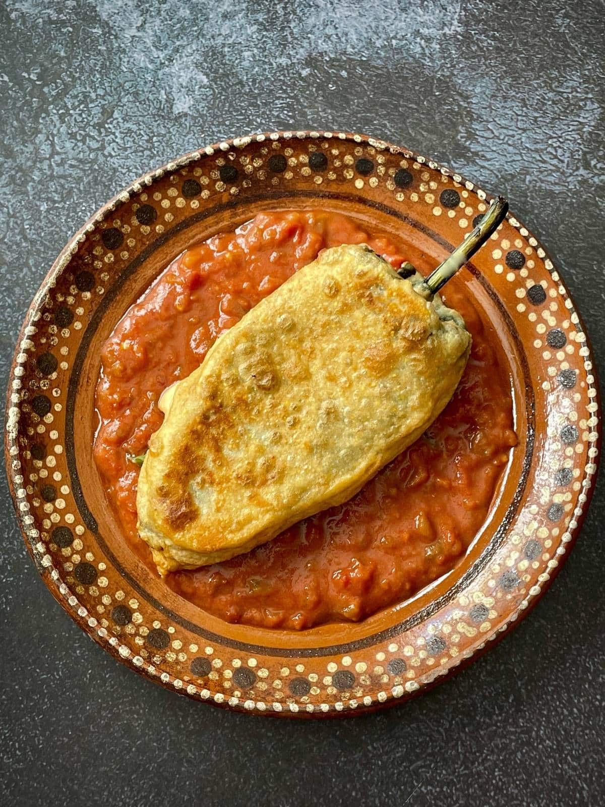 A cooked chile relleno on red chile sauce.