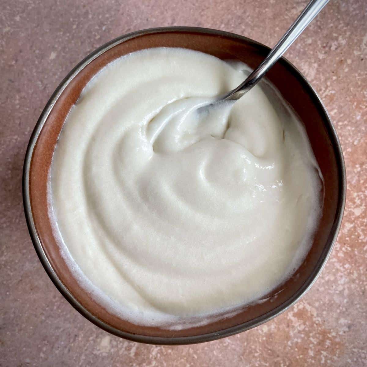 A bowl of vegan cream cheese frosting with a spoon in it.