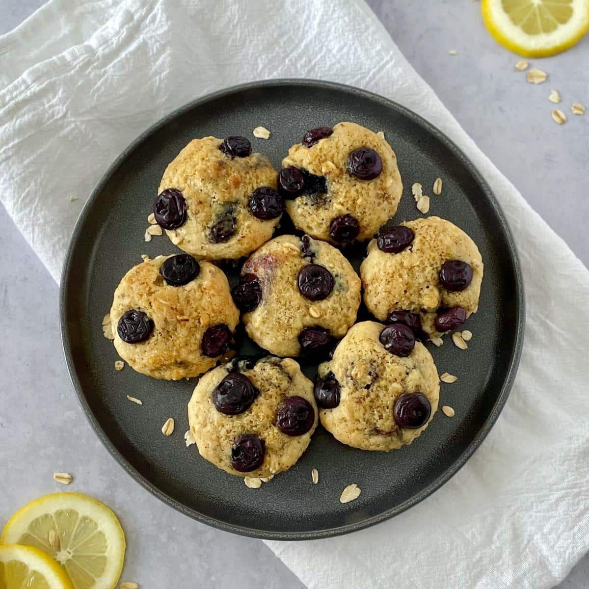 Plate of lemon blueberry muffins over a napkin with lemon slices on the side.