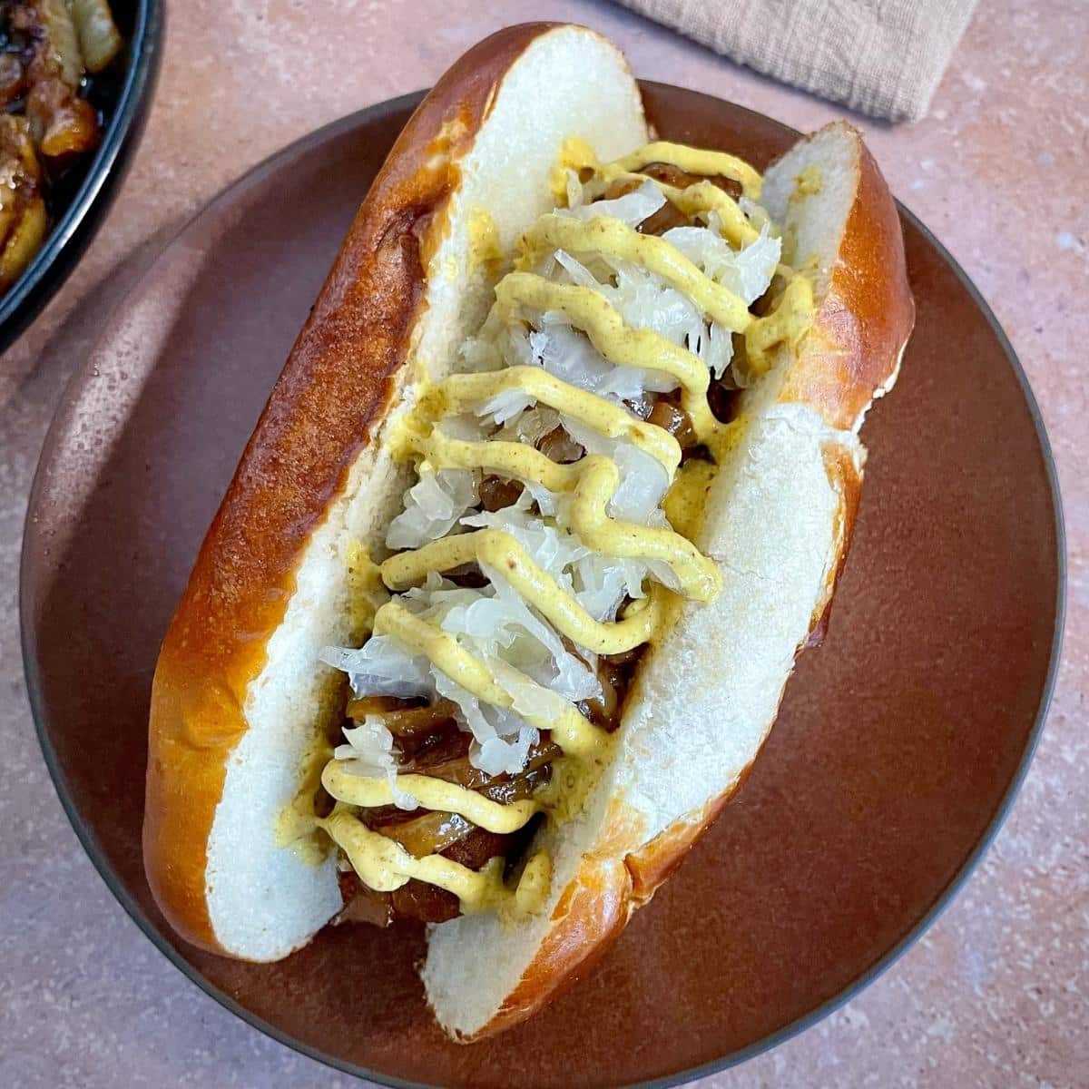 A vegan bratwurst inside a pretzel bun, topped with sauerkraut, onions, and spicy mustard.