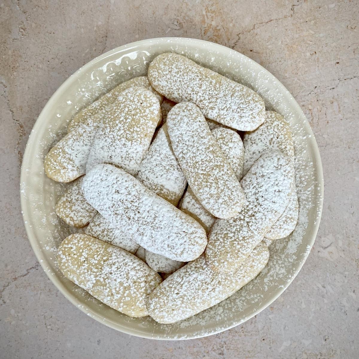 A plate of vegan ladyfingers with powdered sugar.