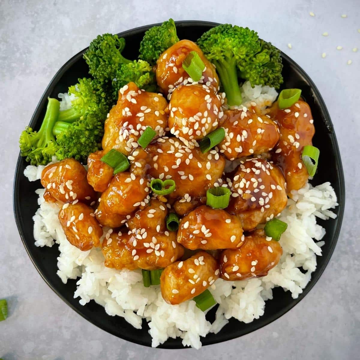 Plate of vegan sesame chicken on top of rice and broccoli.