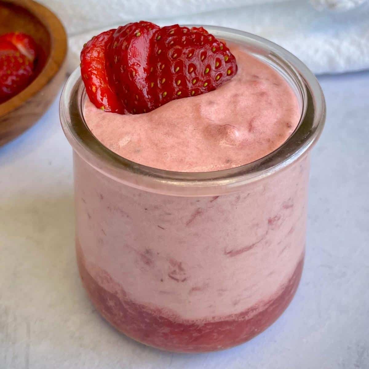 A jar of vegan strawberry mousse, topped with strawberries.