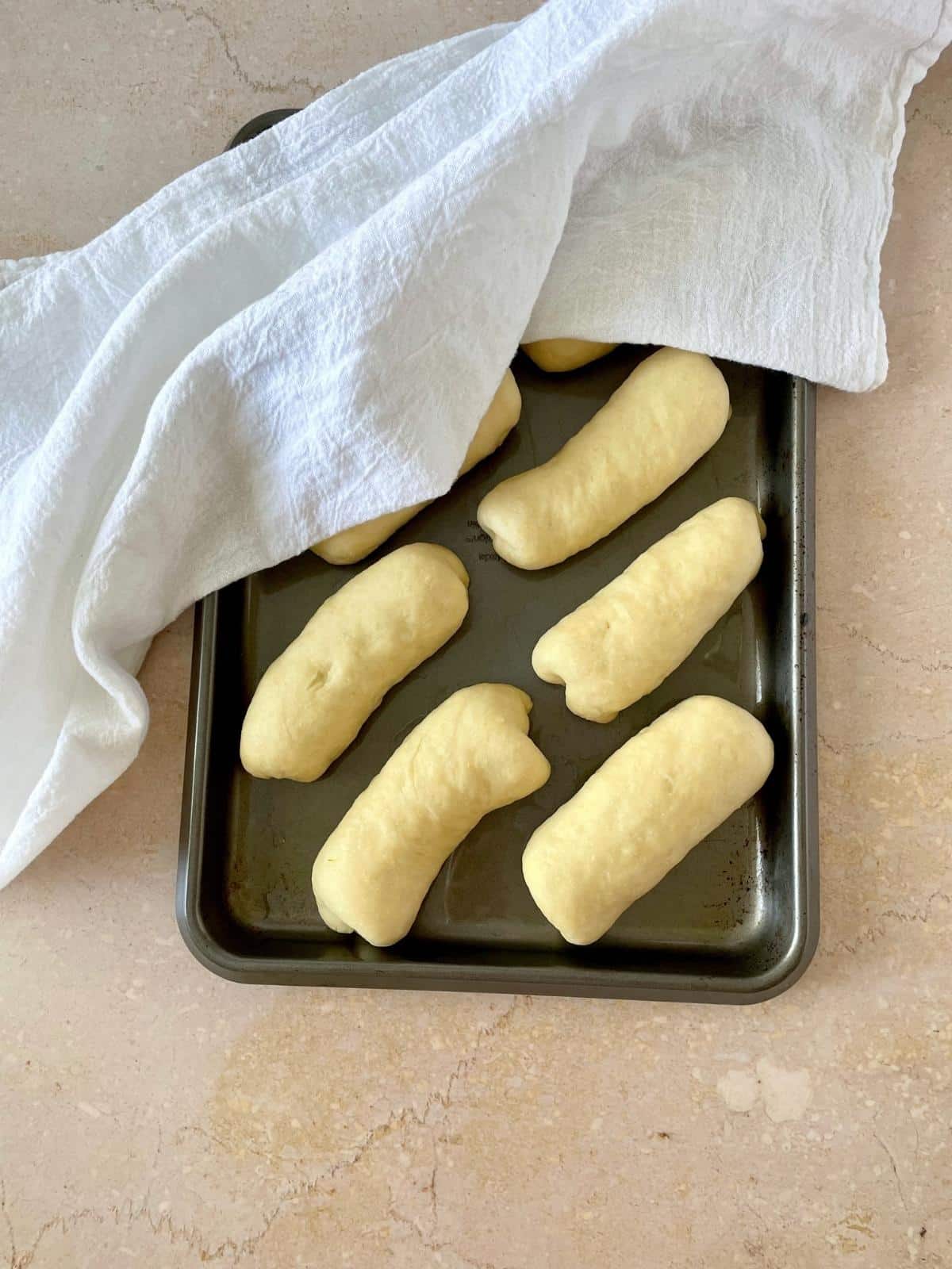 Covered rolls rising on a sheet pan.