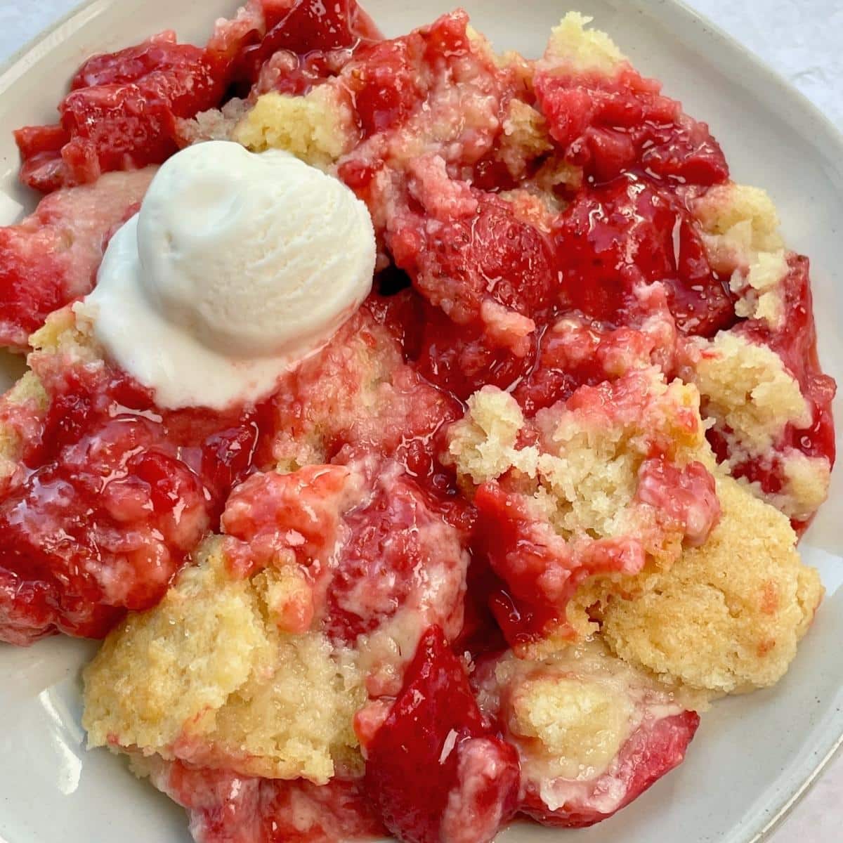 A plate of vegan strawberry cobbler with ice cream on top.