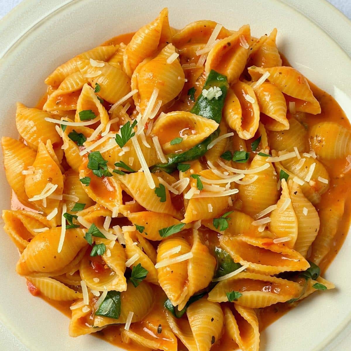 A plate of creamy vegan tomato pasta garnished with parsley.