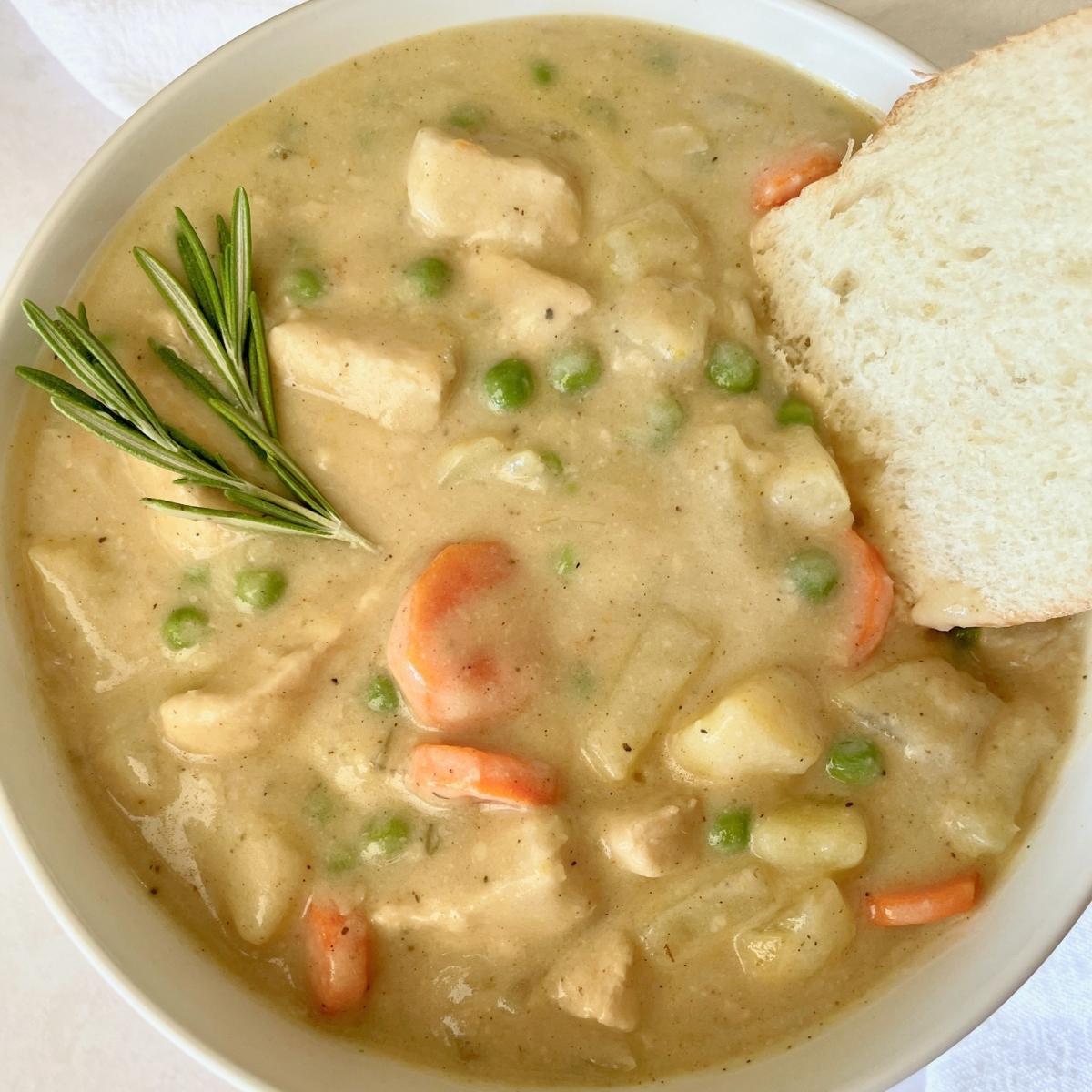 A bowl of pot pie soup with rosemary and bread.