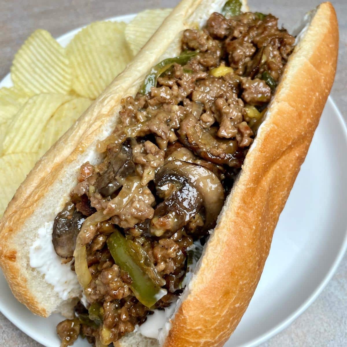 A vegan Philly cheesesteak sandwich with chips on the side.