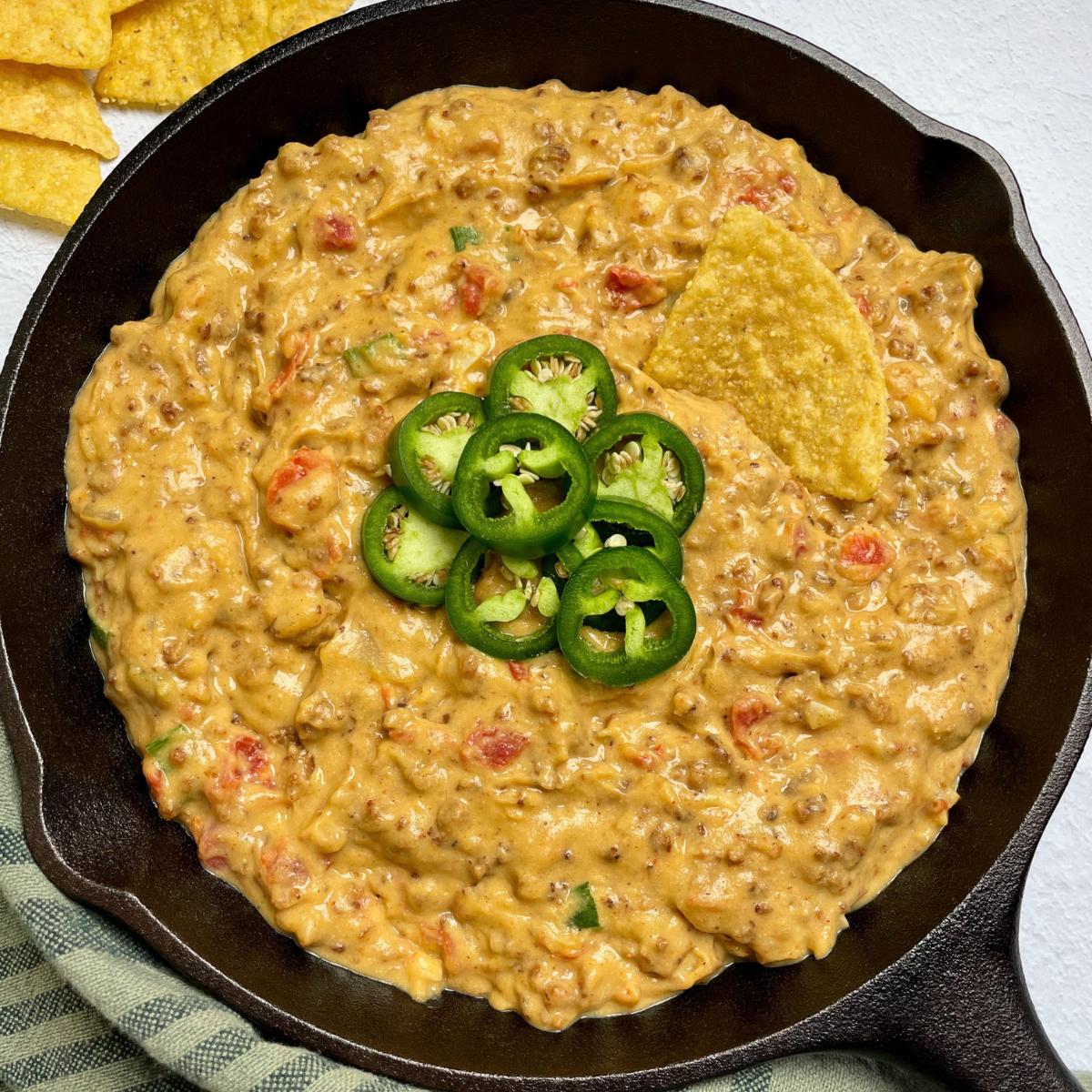 A skillet with vegan cheese dip and jalapeños.