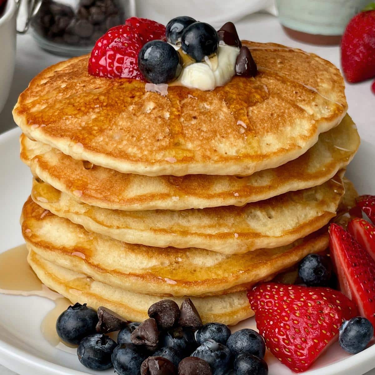 A stack of vegan buttermilk pancakes with syrup and fruit.