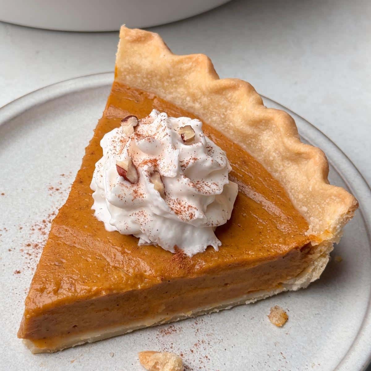 A slice of vegan pumpkin pie with whipped cream and nuts on top.